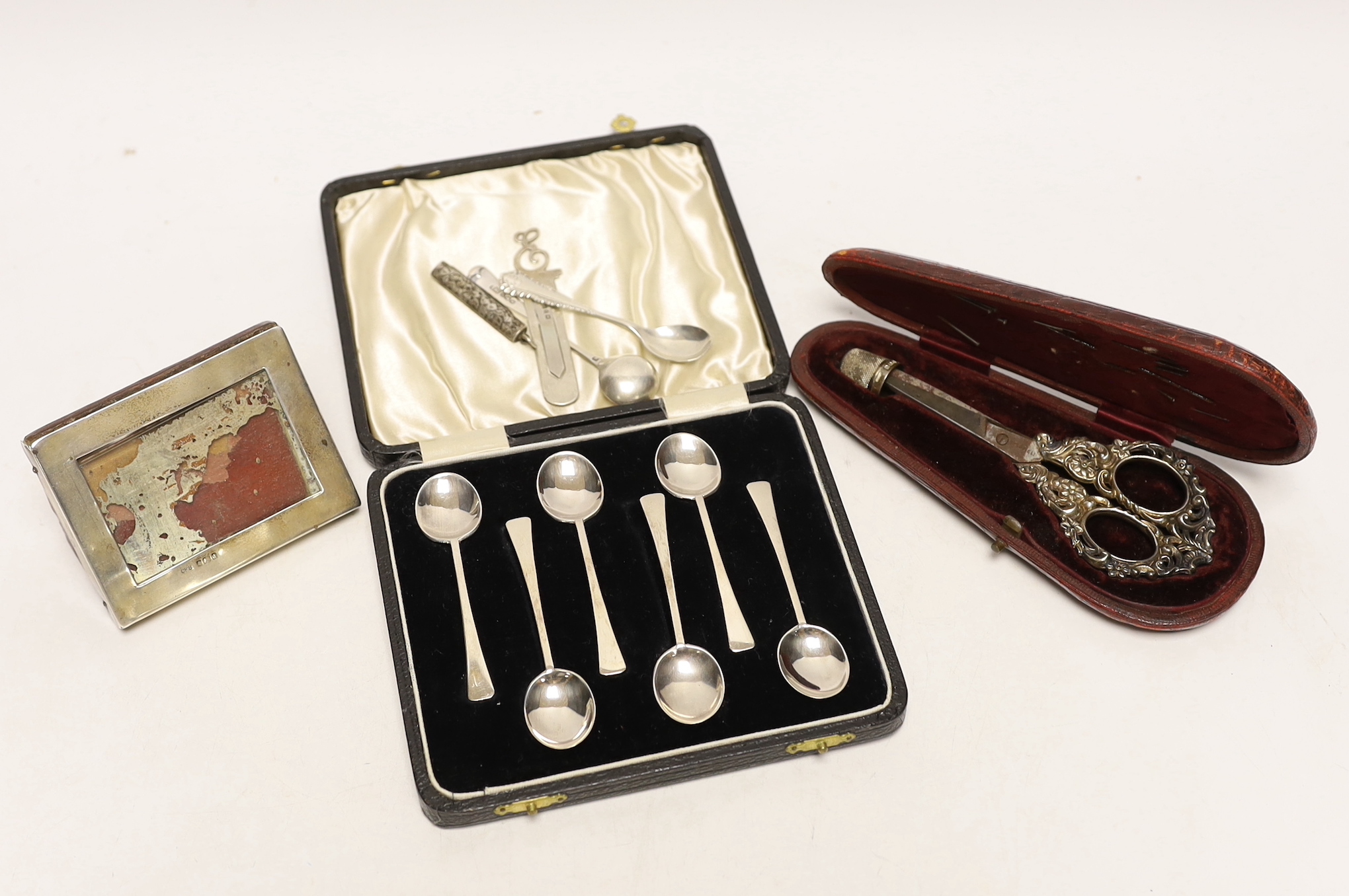 A cased pair of late Victorian repousse silver handled scissors and later silver thimble, a silver mounted photograph frame, cased set of six silver coffee spoons, bookmark, penknife and two condiment spoons.